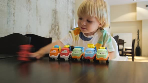 Happy Child Has Fun Playing with a Colorful Car at Table in a Restaurant