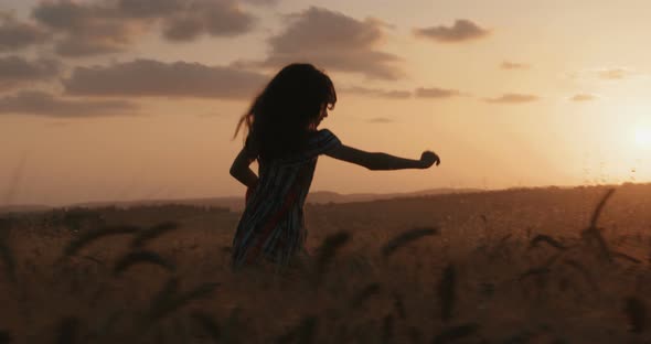 young girl in a golden field during sunset raising her hands in happiness