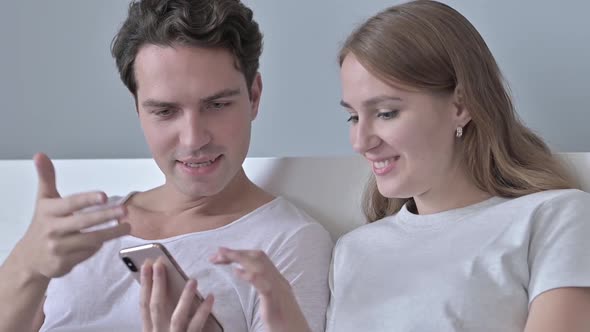 Cheerful Couple Sitting in Bed and Using Smartphone