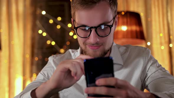 Handsome Bearded Man Using a Smartphone and Smiling While Drinking Beer in Pub