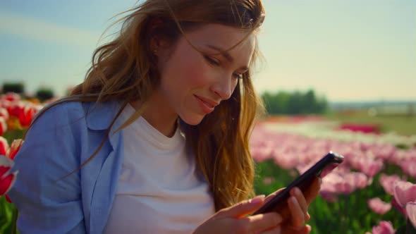 Young Lady Sending Kisses Online Via Mobile Phone While Walk in Flower Park