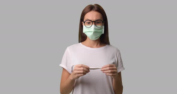 Brunette Woman in Medical Mask and Glasses Checking Her Temperature Isolated Over White Bg