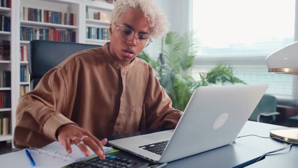 Young African American Woman Counts on Calculator and Keeps Home Accounting