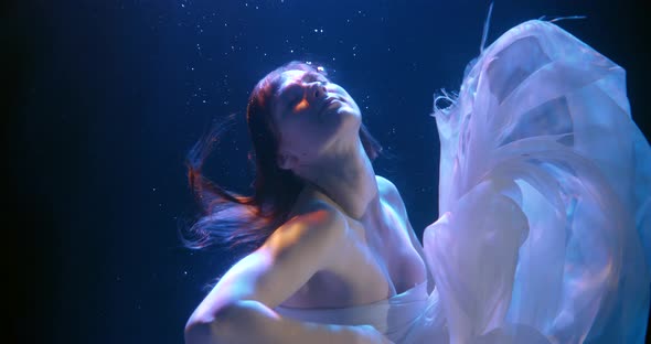 Tender Woman Dressed in White Silk Gown Is Floating Underwater in Night, Slow Motion