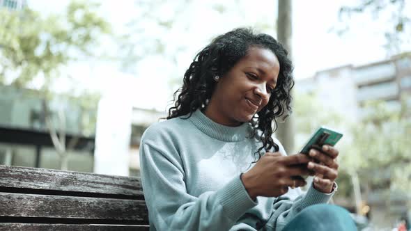 Happy brunette African woman wearing blue sweater typing by mobile