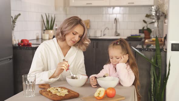 Young Happy Family Mother and Little Daughter Sitting at the Kitchen Table Smiling Enjoying