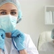 Female Doctor Corrects Mask on Background of Colleagues at Computer in Clinic - VideoHive Item for Sale