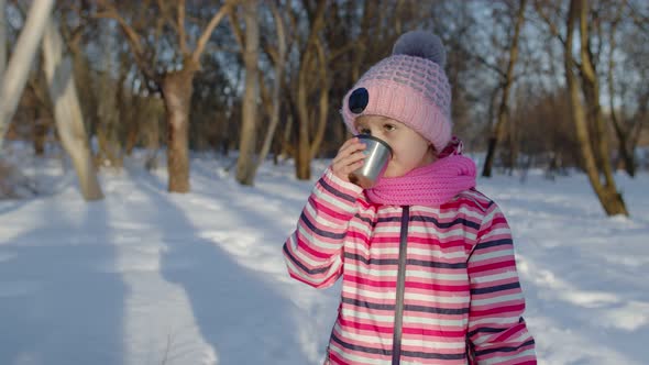 Smiling Child Kid Girl Drinking Hot Drink Tea From Cup Trying To Keep Warm in Winter Park Forest