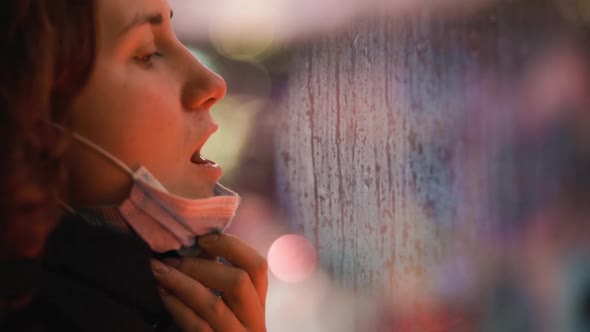 Young Woman in Medical Mask Breathes on Window and Writes 2021