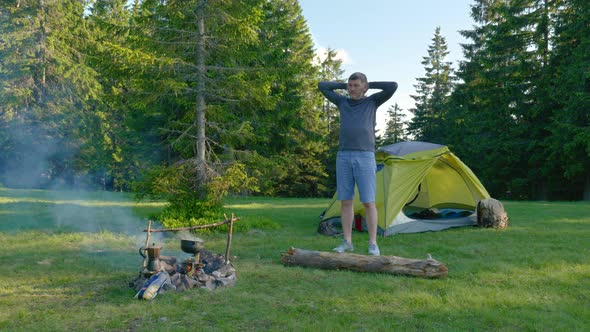 Bearded Man Near Campfire and Tent in the Mountains