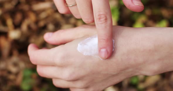 close-up of a hand smears a white cream on a background of greenery. Hand skin care