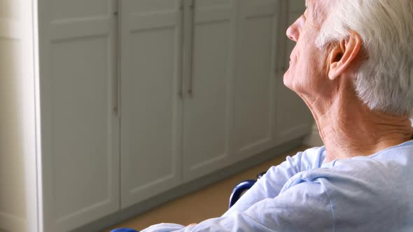 Senior man sitting in wheelchair looking through window in bedroom