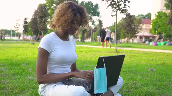 Young African American Woman Using Laptop in Park During Covid 19 Pandemic. Medical Disposable Mask