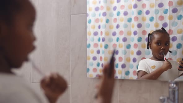 Cute African Preschool Girl Brushing Teeth and Using Smartphone in Bathroom