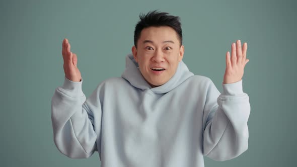 Surprised Asian man wearing hoodie rejoicing at the camera