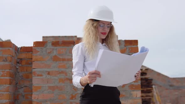 A Female Architect in Business Attire Stands on the Top Floor in the Open Air at a Construction Site