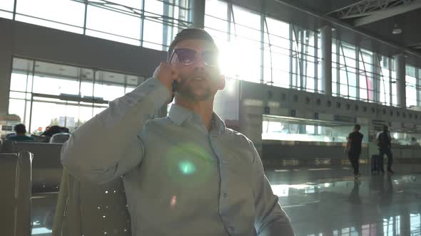 Young Businessman Talking on Phone at Airport with Sun Flare at Background