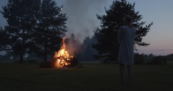 Natural Woman Wearing Dress Looking at Bonfire at Summer Night