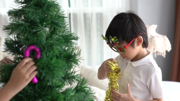 Asian Child Hanging Decorative Toy Together On Christmas Tree