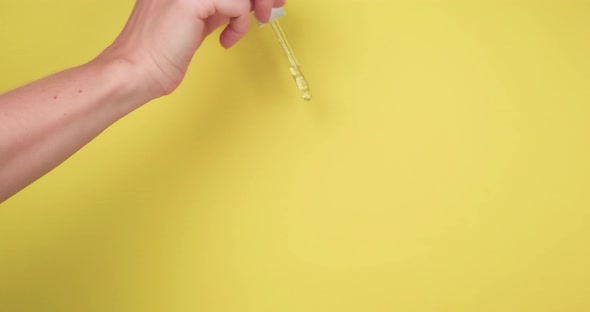 Female hand pouring out serum of pipette on yellow background