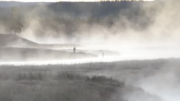 Wide view of 2 people through steam coming off winding river