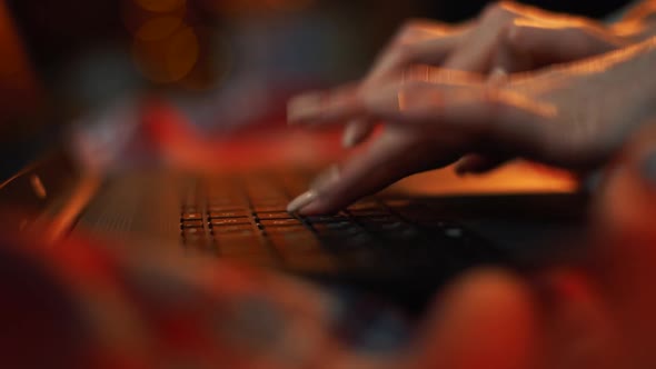 Close-up Hands of Unrecognizable Woman Typing on Laptop Keyboard at Room with Dark Red Lighting.