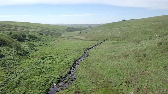 Wide aerial shot tracking forward, with wistmans wood, a river and grassy moorland setting the scene