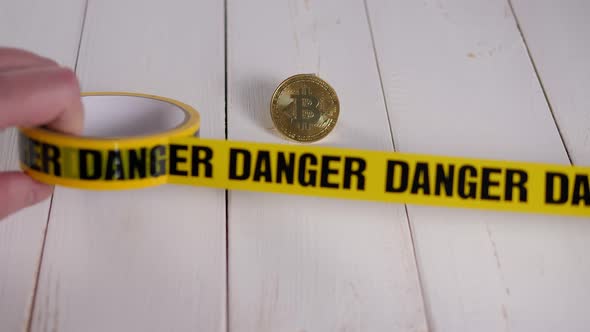 Closeup of a Bitcoin Coin with a Yellow Warning Tape with the Inscription DANGER