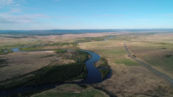 Aerial View of a River Flowing Through Rural Area with Meadows Rare Trees and with the Road on the