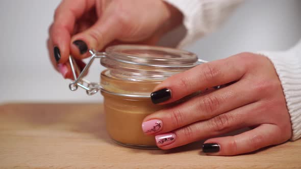 Girl opens a glass jar with homemade juicy peanut butter
