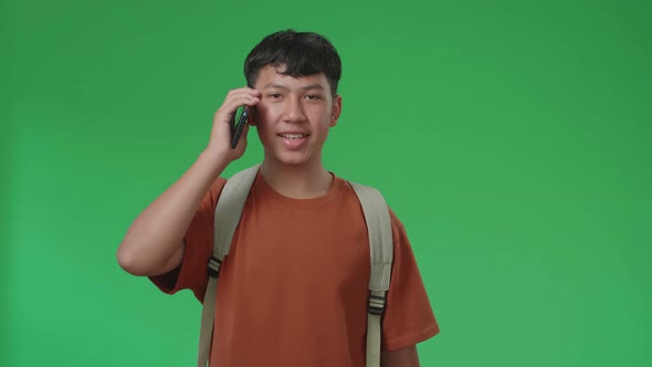 The Front View Of Asian Boy Student Talking On Mobile Phone While Walking On Green Screen Chroma Key