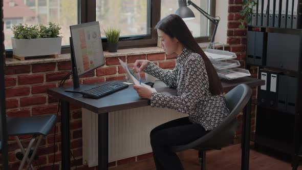 Asian Woman Comparing Charts on Papers and Computer