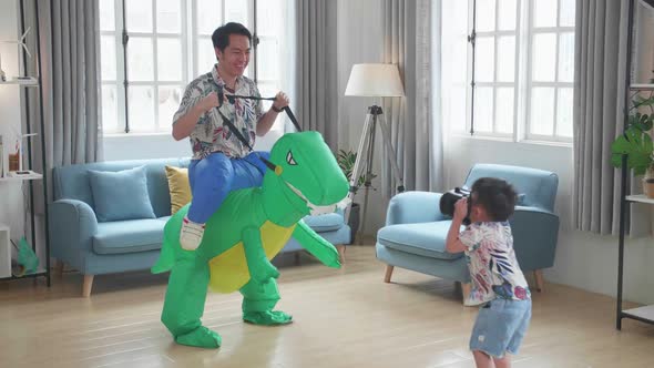 Father Ride Dinosaur Toy While His Son Using Vr Headset In Modern House Living Room, Happy Family