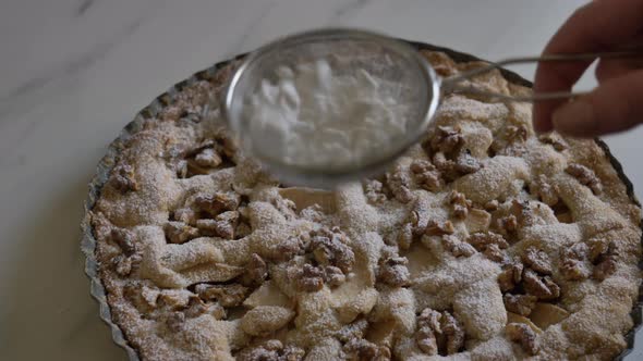 woman sprinkles icing sugar on nut pie on table at home