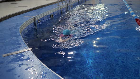 Little Girl in Swimsuit Cap and Goggles is Diving and Swimming to Egge of Pool