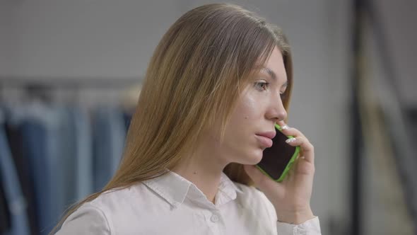 Headshot Laughing Young Woman Standing in Clothes Shop Talking on Smartphone