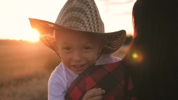 Happy Little Toddler Boy in Hat Having Fun Sitting in Parents Arms in Field in Summer at Sunset