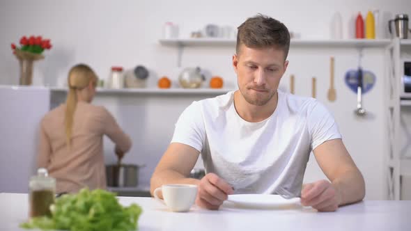 Hungry Man Eagerly Waiting for Dinner, Wife Cooking on Background, Starvation