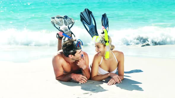 Couple wearing diving mask and flippers lying on beach