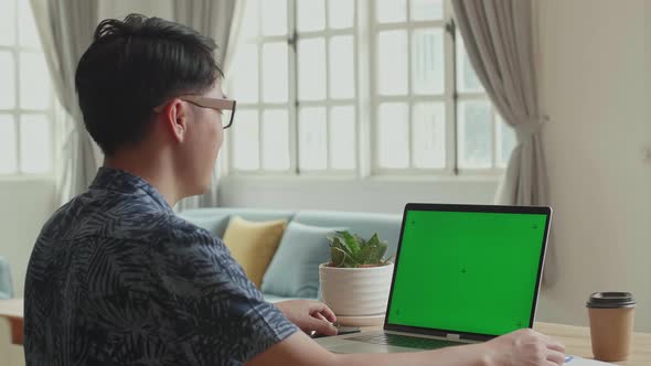 Man Waving Hand During Video Call On Laptop Computer With Green Screen Display At Home