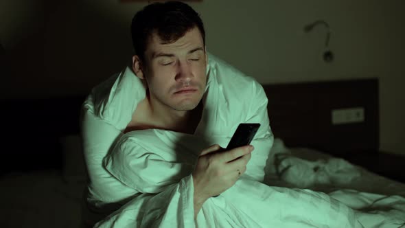 Young Man Wrapped in Blanket Sitting on Bed and Watching Tv