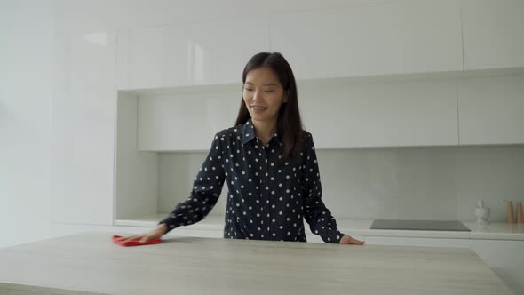 Asian Woman Cleans and Wipes the Table with a Microfiber Cloth in the Kitchen