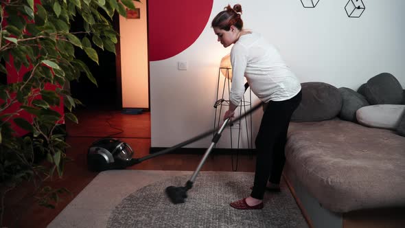Tired Pregnant Woman Vacuum-cleans in a Room