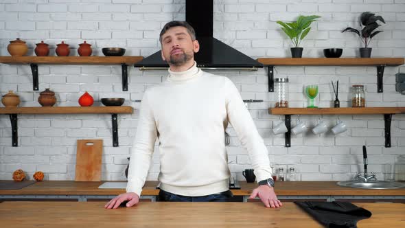 Pensive man stands in home kitchen near table looking up with open mouth