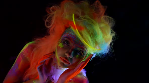 Sexy Lady with Creative Fluorescent Makeup and Body Art Glowing in Darkness with UV Lights