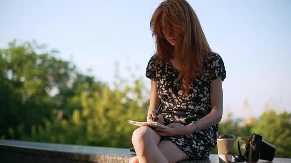 Ginger Beautiful Teen Girl Sitting Writing Notes with Coffee to Go and Film Camera in Slowmotion