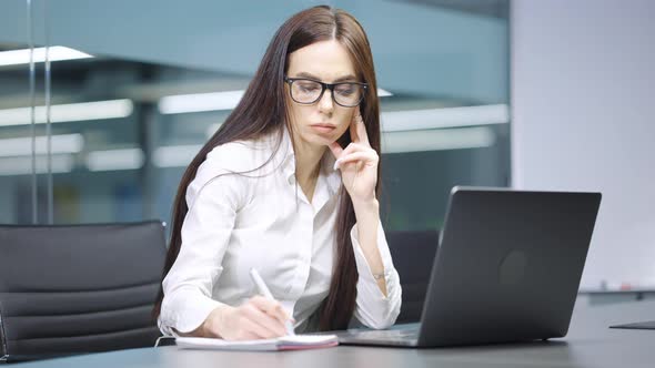 Businesswoman Writing in Journal and Using Laptop