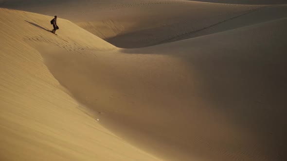 Man Walking On Sand Dunes Through Desert