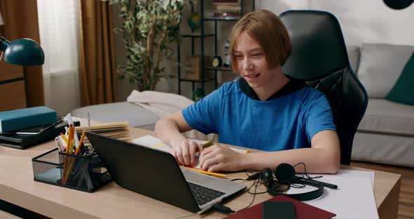 Elementary School Boy Has Lesson with Teacher Remotely Over Internet Child Waves to Laptop Camera to alt