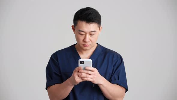 Concentrated Asian doctor texting by phone